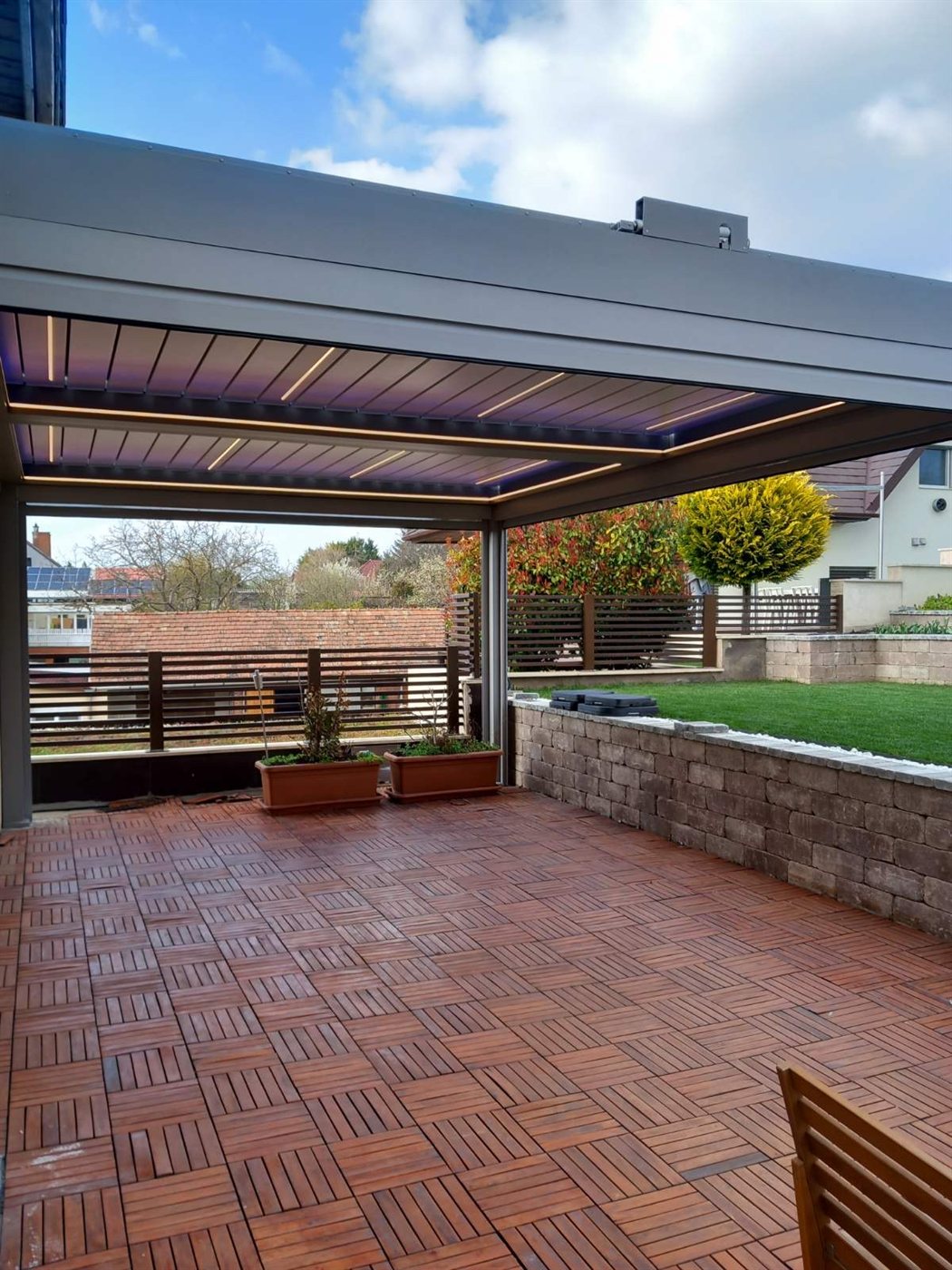 Pergola meleg lamellavilágítással, fa burkolatú terasz és gondozott kert