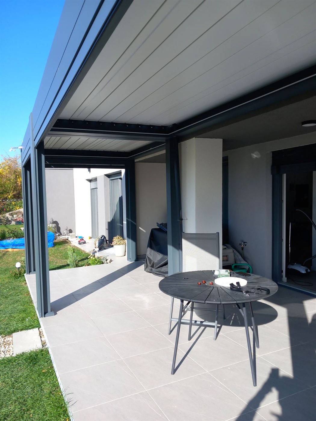 Kilátás a pergola alól: lamellás tető és tágas burkolt terasz