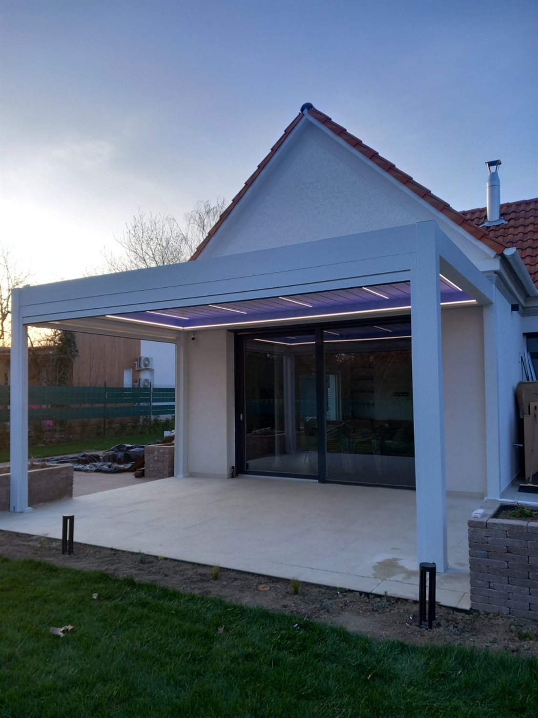 Fehér keretes pergola lila lamellavilágítással, alkonyatban